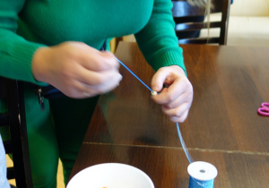 Kobieta wykonuje bransoletkę nawlekając na sznurek koraliki