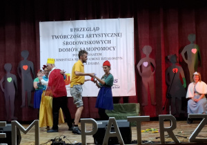 Grupa osób na scenie występujących w przedstawieniu.