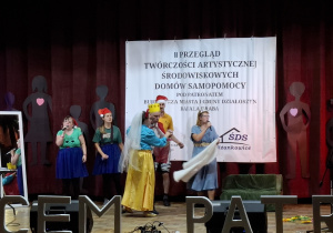 Grupa osób na scenie występujących w przedstawieniu.
