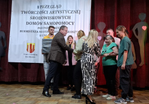 Grupa osób na scenie. Grupa odbiera gratulację i pamiątkowy dyplom za swój występ.