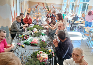 Grupa osób siedzących przy stole. Wszyscy wykonują palmy wielkanocne.