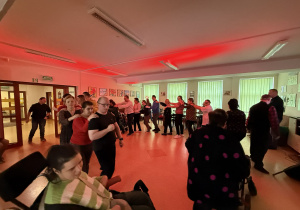 Grupa osób tańczy trzymając się za ramiona, tworząc wężyk.