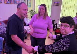 Dwie kobiety i mężczyzna tańczą w kółku trzymając się za ręce.