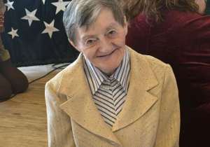 Uśmiechnięta kobieta w jasnym żakiecie siedzi przy stole.