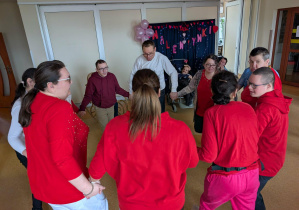 Grupa osób ubranych na czerwono tańczy w kółku trzymając się za ręce.