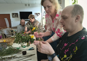 Kilka osób tworzy palmy wielkanocne.