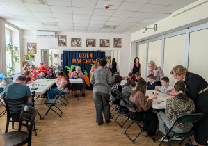 Grupy osób wykonujące prace rękodzielnicze w postaci marchewkowych breloczków.