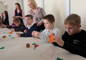 Kilka osób przy stole wykonuje breloczki w kształcie marchewki.
