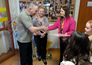 Grupa osób wita się przekazując sobie preznt.