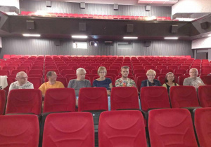 Osiem osób kobiet i mężczyzn siedzących w jednym rzędzie na czerwonych fotelach w kinie