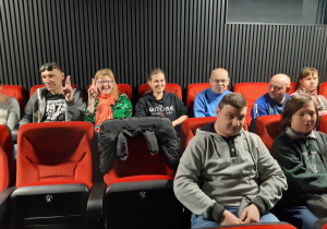 Osiem osób siedzi na czerwonych fotelach w kinie