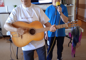 Dwóch mężczyznw kapeluszach jeden z gitarą drugi z mikrofonem