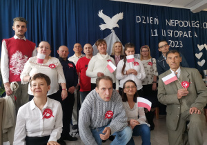 Grupa osób pozuje do zdjęcia. W dłoniach trzymane są flagi narodowe a na piersi widnieją biało-czerwone kotyliony.