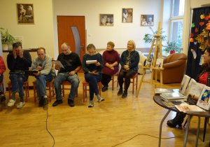 Grupa osób siedzących na krzesłach czyta fragmenty teksów z książek