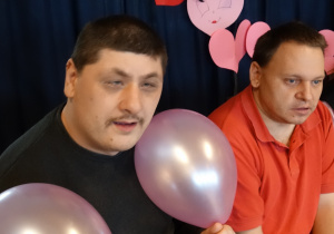 Dwóch chłopców z balonami siedząych na ławce na tle napisu "Walentynki"