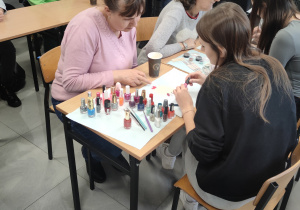 Grupa kobiet siedzących przy stoliku maluje paznokcie