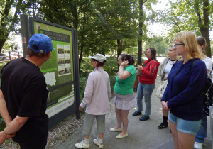 Grupa osób w parku wpatrujących się w tablicę informacyjną.
