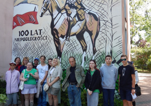 Grupa osób na tle muralu z rycerzem na koniu.