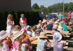 Duża liczba dzieci siedzących przy drewnianych stolikach.